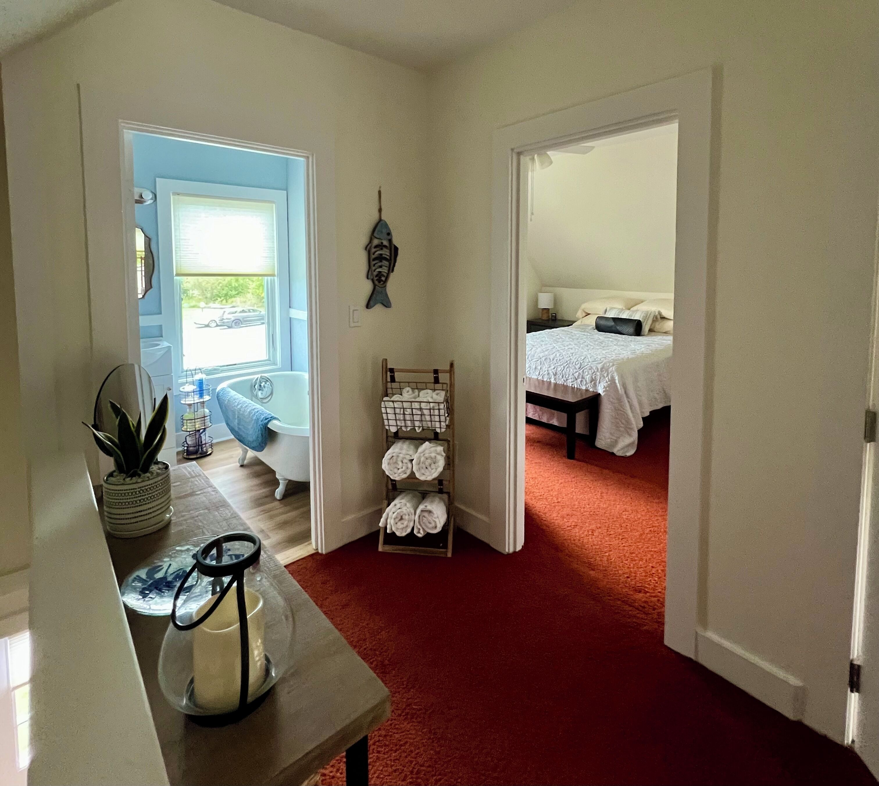 A room with a red carpet, a bathtub, a bed with white bedding, and a wall-mounted fish decoration.