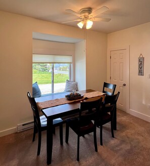 A dining area with a table, chairs, a ceiling fan, and a view through a window.