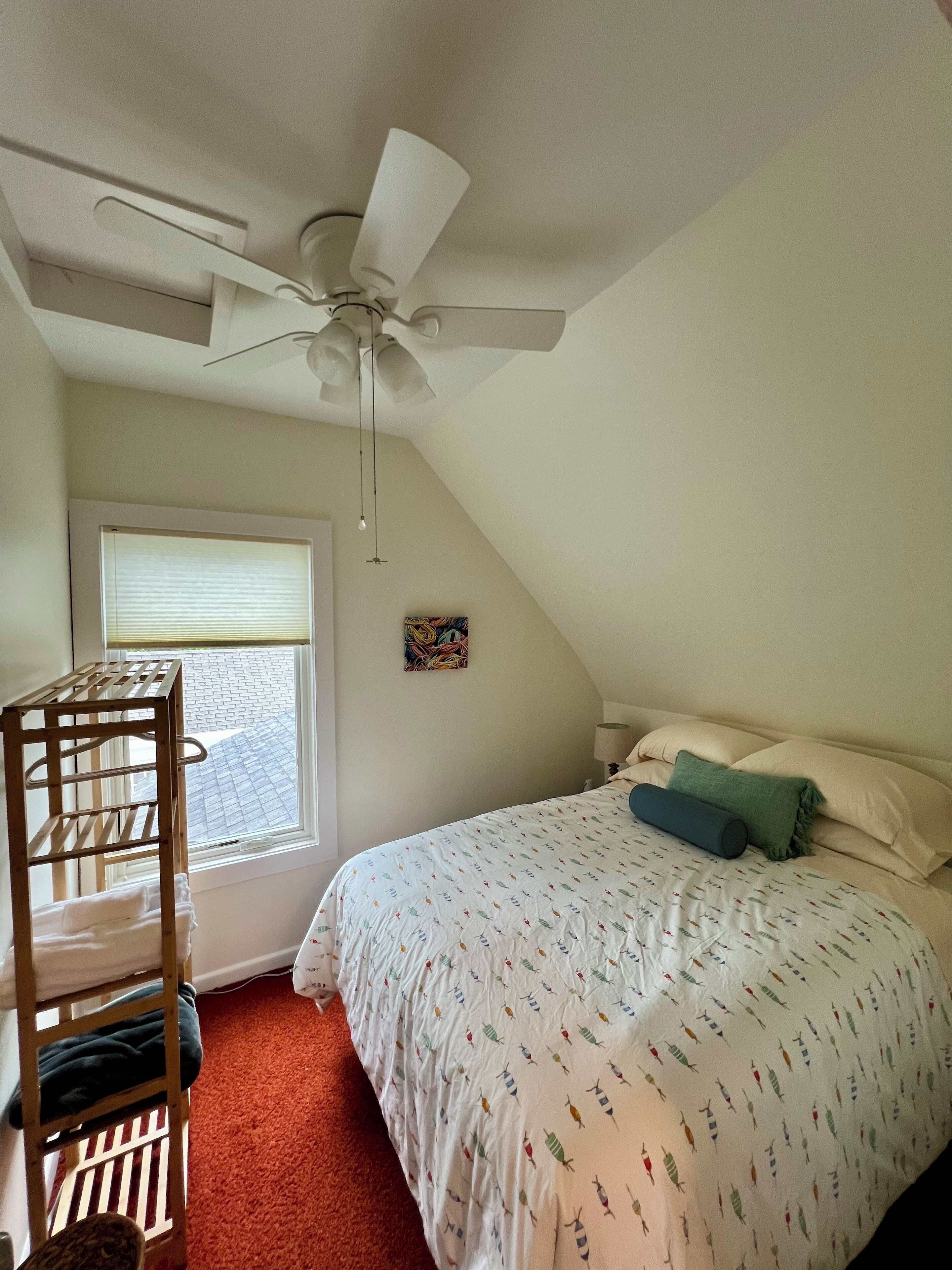 A bedroom with a bunk bed, a ceiling fan, a window with blinds, and a bed with patterned bedding.