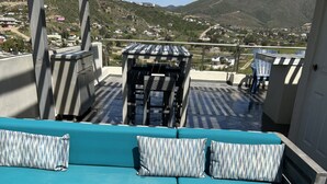 A rooftop terrace with a teal sofa set, a small table, and a grill. - Comfortable safe gated community, located 12 min away from Valle de Guadalupe. (El Sauzal)