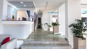 Un moderno vestíbulo de hotel con un mostrador de recepción, zona de estar y una escalera que sube a los pisos superiores.