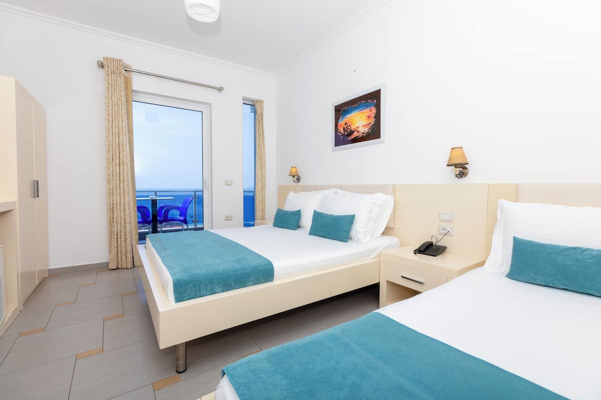 A hotel room with two beds, a balcony, a painting, and a phone on the nightstand.