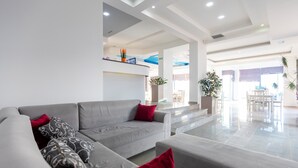 Un salón moderno con un sofá gris, cojines rojos y estampados, y un espacio luminoso y despejado con luz natural.
