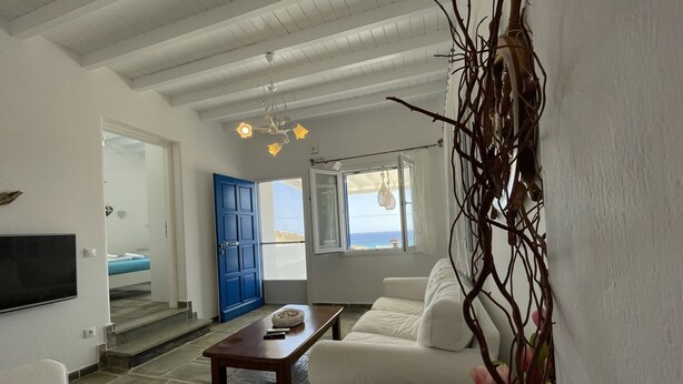 A modern living room with a white sofa, a wooden coffee table, and a TV mounted on the wall. - Venus - Venus Myconian Residences (Cyclades)