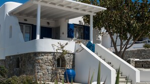A modern white building with a stone facade, a blue door, and a staircase leading to a covered area. - Venus - Venus Myconian Residences (Cyclades)