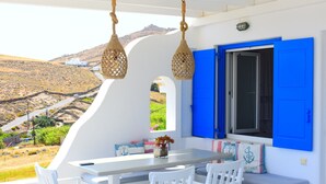 A white table with chairs, a blue shuttered window, and a view of a hilly landscape. - Venus - Venus Myconian Residences (Cyclades)