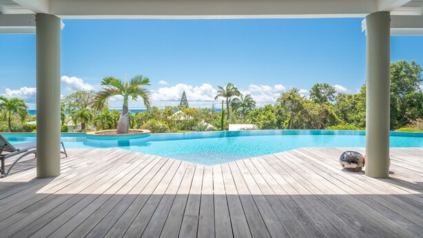 Eine Holzterrasse mit Schwimmbad, Palmen und Blick auf den Ozean.