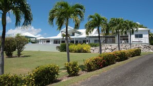 Ein modernes Resort mit einem weißen Gebäude, Palmen und einem gepflegten Rasen.
