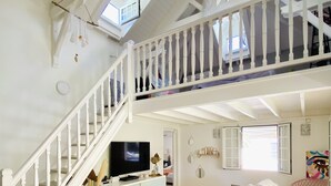 Ein großzügiger Wohnbereich mit hohen Decken, einer Treppe, einem Fernseher, einer Couch und einem Essbereich.