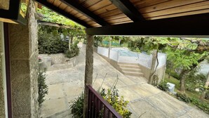 A covered outdoor area with stone steps leading to a pool, surrounded by greenery and a white fence.