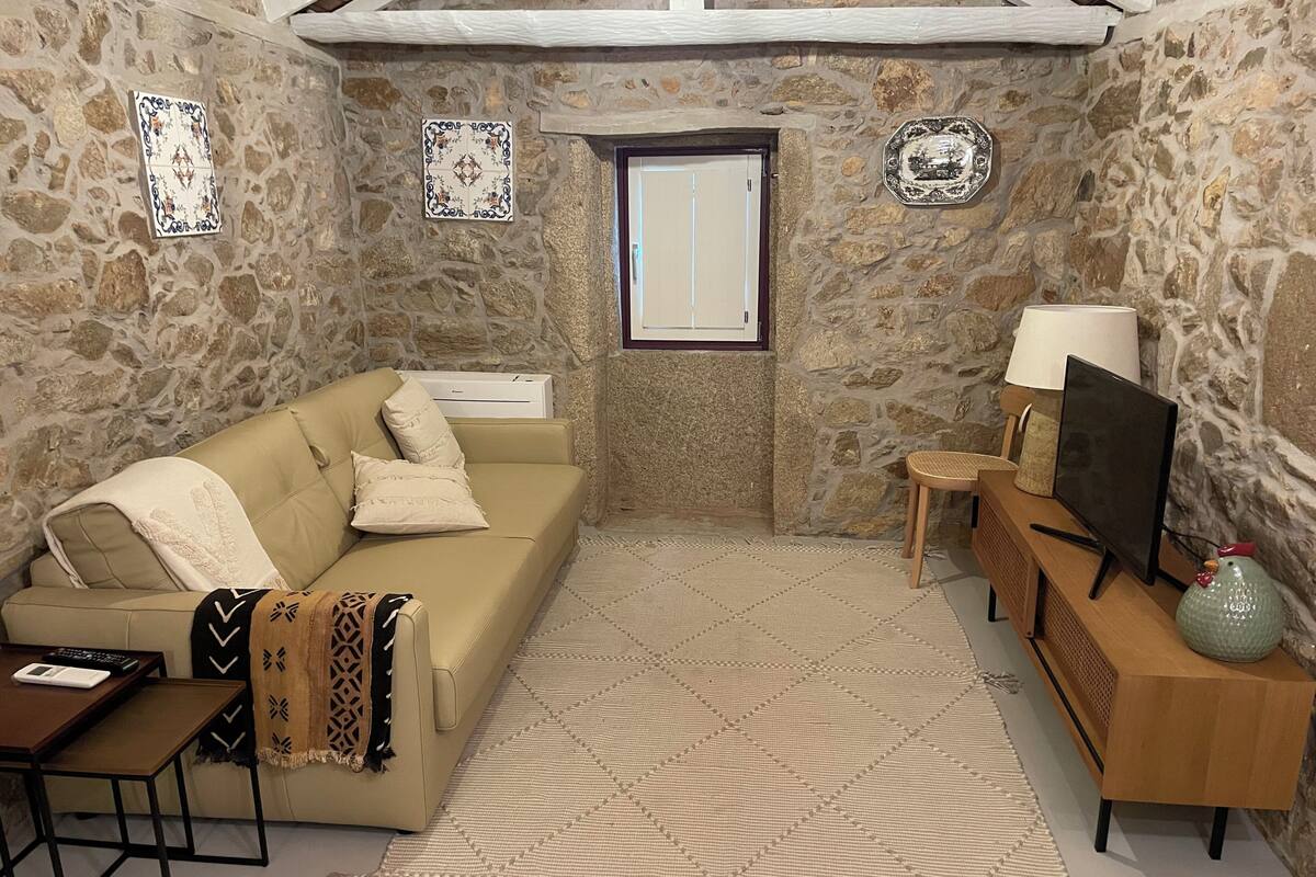A stone-walled room with a beige sofa, a small table, a TV, and a decorative vase.