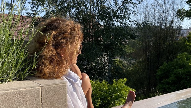 A person sitting by a pool with a garden view.