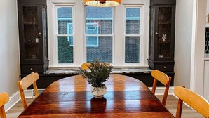 Une salle à manger avec une grande table en bois, une plante en pot et un luminaire suspendu.