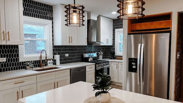 Une cuisine moderne avec des armoires blanches, un réfrigérateur en acier inoxydable et des luminaires suspendus.