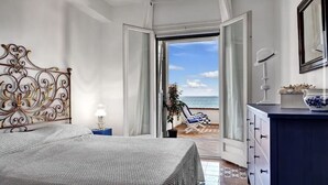 A bedroom with a bed, a nightstand, a dresser, and a view of the beach. - Raffaela's House (Massa Lubrense)