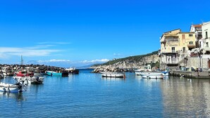A coastal marina with boats docked, clear blue water, and buildings along the shore. - Raffaela's House (Massa Lubrense)