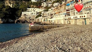 A coastal town with buildings on a hillside, a pebble beach, and a red heart symbol. - Raffaela's House (Massa Lubrense)