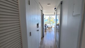 Un corridoio con pavimento in legno, pareti bianche e vista su una stanza con un letto e una finestra.
