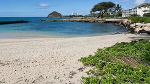 Una spiaggia con acque cristalline, una riva sabbiosa e un edificio con facciata bianca sullo sfondo.