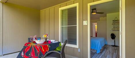 A room with a dining table set for two, a chair, and a bed with a blue cover.