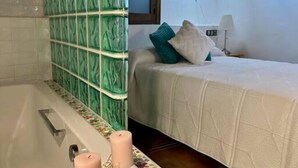 Um banheiro com banheira, parede com azulejos verdes e cama com colcha branca e azul-turquesa.