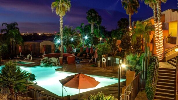 Een zwembadgedeelte van een resort bij nacht, met palmbomen, ligbedden en een trap.