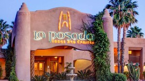 Het exterieur van La Posada, een hotel met een opvallende ingang, een stenen fontein en palmbomen.