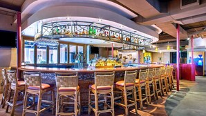 Een bar met een gebogen toonbank, rieten barkrukken en diverse flessen en glazen.