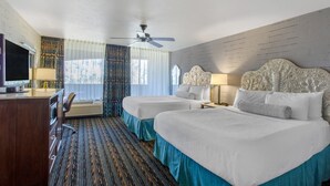 Een hotelkamer met twee bedden, een bureau met een televisie, een plafondventilator en een raam met gordijnen.
