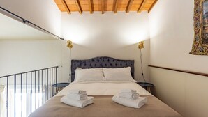 A hotel room with a bed, two bedside tables, a balcony, and a painting on the wall.