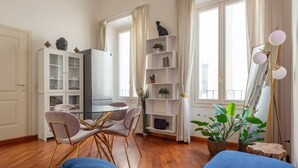 A modern living room with a blue sofa, a dining table with chairs, a white cabinet, and a mirror with a stand.