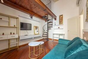 Een woonkamer met een bank, een televisie, een spiltrap en een witte console tafel.