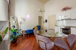 Een moderne woonruimte met een glazen eettafel, paarse stoelen, een blauwe bank, een klein bijzettafeltje en een potplant.
