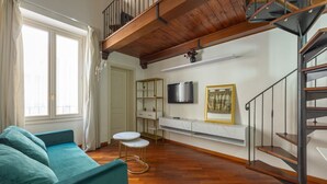 A living room with a sofa, a small table, a TV, a staircase, and a shelf with a picture.