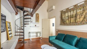 A living room with a spiral staircase, a green sofa, a white table, and a large framed painting.