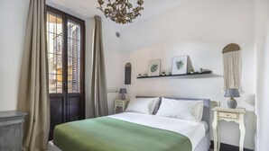 A bedroom with a bed, a nightstand, a dresser, a window with curtains, and a chandelier.