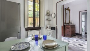 A dining area with a table set for two, a window with a view, a clock, and a mirror on the wall.