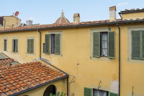 Un bâtiment jaune avec des volets verts, un toit en tuiles et un dôme en arrière-plan.