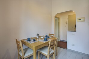 Un espace repas avec une table et des chaises en bois, un coin cuisine avec un comptoir et un évier, et un couloir menant à une autre pièce.