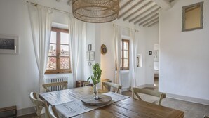A dining area with a wooden table, white curtains, and a hanging rattan light fixture.