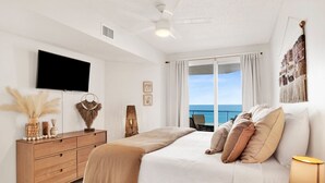 Un dormitorio con cama, televisor, cómoda y vista al océano.