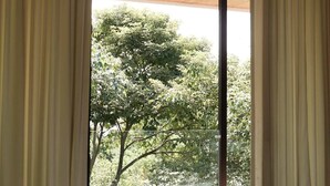 A room with a bed, a ceiling fan, and a view of trees through a window with curtains.
