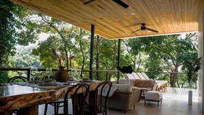 An outdoor dining area with a wooden table and chairs, surrounded by wicker furniture and a ceiling fan.