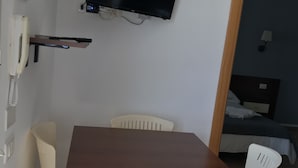 A small room with a wooden table and four white plastic chairs. A flat-screen TV is mounted on the wall above the table. - Apartment by the sea with swimming pool (Porto Empedocle)