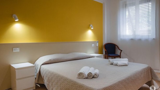 A hotel room with a bed, a nightstand, a chair, and a window with blinds. - Apartment by the sea with swimming pool (Porto Empedocle)