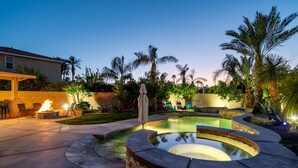 Ein Garten mit Whirlpool, Feuerstelle und Liegestühlen.