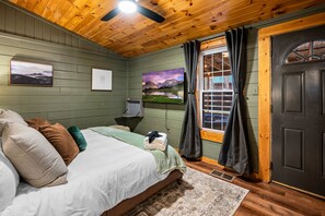 A bedroom with a bed, pillows, a TV, a window with curtains, and a door.