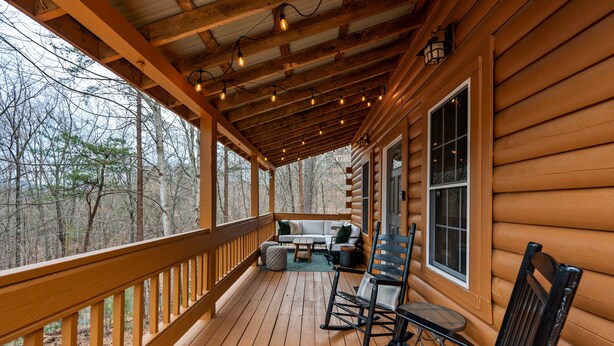 Een houten chalet met een overdekte veranda, ingericht met een bank, stoelen en een tafel.