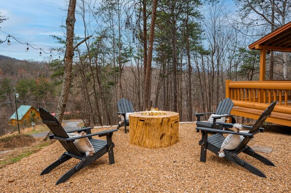 A wooden deck with Adirondack chairs, a fire pit, and a view of a forested area.