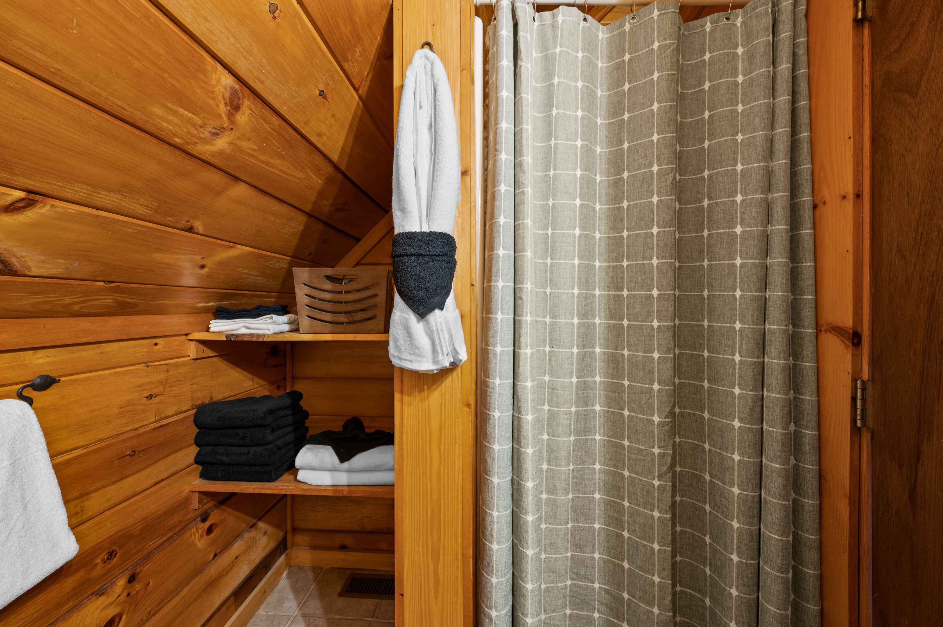 A wooden cabin interior with a wooden shelf holding folded towels and a hanging towel.